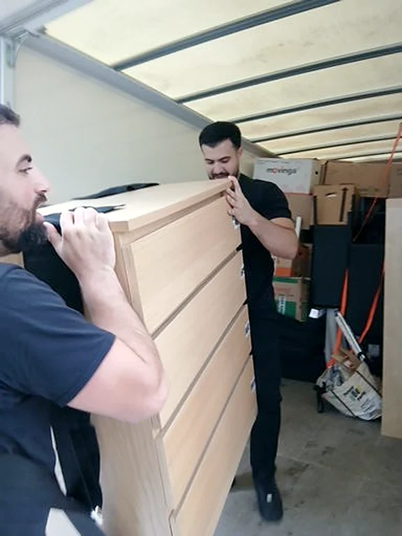Helfer verladen eine Kommode in den Umzugswagen
