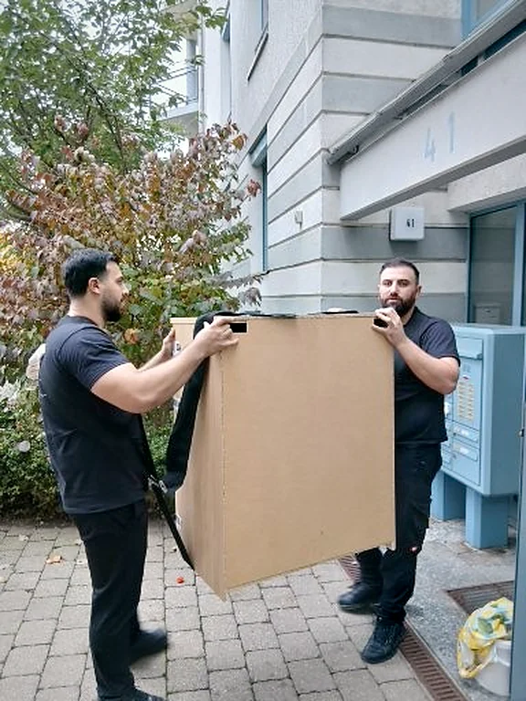 Zwei Umzugshelfer von Two Spears tragen einen Schrank vor dem Haus