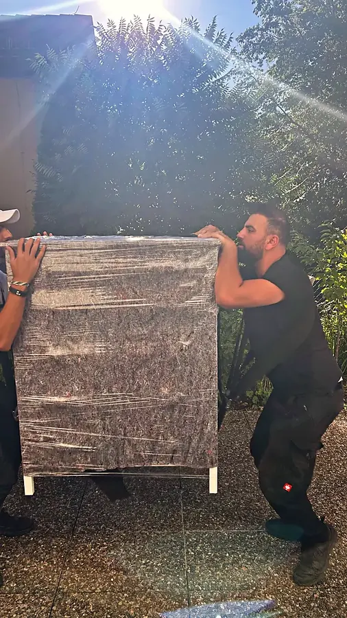 Zwei Mitarbeiter tragen eine verpackte Kommode im Freien